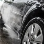 高圧洗浄機で黒い車のボディを洗車している様子